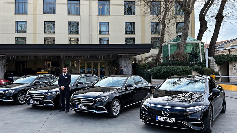 A chauffeur in a suit with black Mercedes S-Class, E-Class and EQS cars in front of a hotel